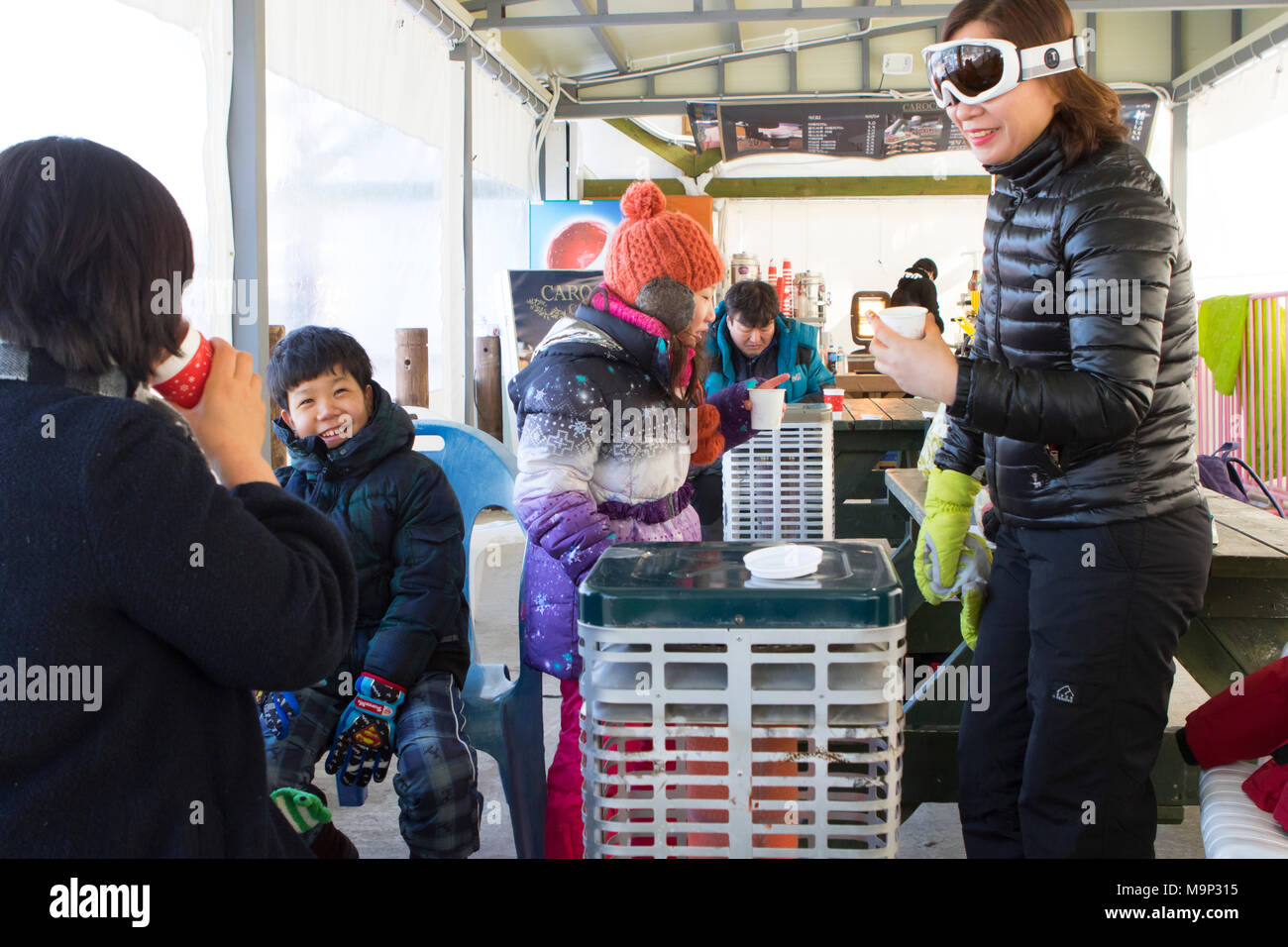 Eine Asiatische suchen Familie befindet sich in der Aufwärmphase in einem Zelt, neben einer Heizung mit heißer Schokolade. Das Yongpyong-resort (Dragon Valley) Ski Resort ist ein Skigebiet in Südkorea, in Daegwallyeong-myeon, Pyeongchang, Gangwon-do. Es ist die größte Ski- und Snowboard Resorts in Korea. Das Yongpyong-resort bewirten die technischen Ski alpin Veranstaltungen für die olympischen Winterspiele und Paralympics 2018 in Pyeongchang. Einige Szenen der 2002 Korean Broadcasting System drama Winter Sonata wurden im Resort gedreht. Stockfoto