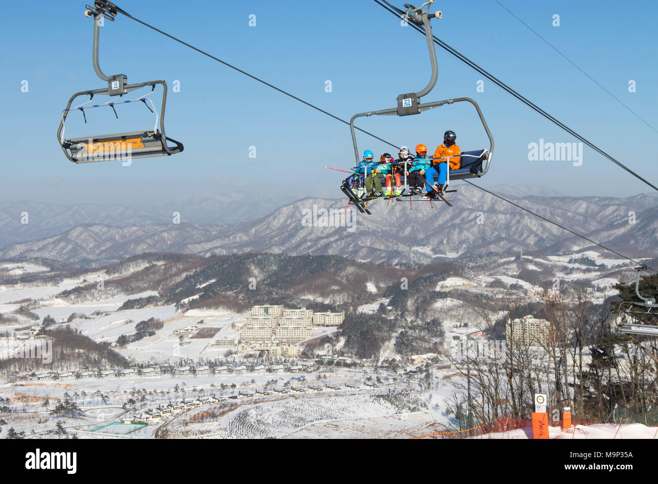 Bunt gekleideter Skifahrer in einem Sessellift hoch über Alpensia Resort in der Region Gangwon-do in Südkorea. Die alpensia Resort ist ein Skigebiet und eine touristische Attraktion. Es ist auf dem Gebiet der Gemeinde von daegwallyeong-myeon befindet sich in der Grafschaft von Pyeongchang, die Olympischen Winterspiele hosting im Februar 2018. Das Skigebiet ist ca. 2,5 Stunden von Seoul oder Incheon Airport mit dem Auto, überwiegend alle Autobahn. Alpensia hat sechs Pisten für Ski und Snowboard, mit bis zu 1,4 km (0.87 mi) lang, für Anfänger und Fortgeschrittene, und ein Bereich für Snowboarder vorbehalten. Stockfoto