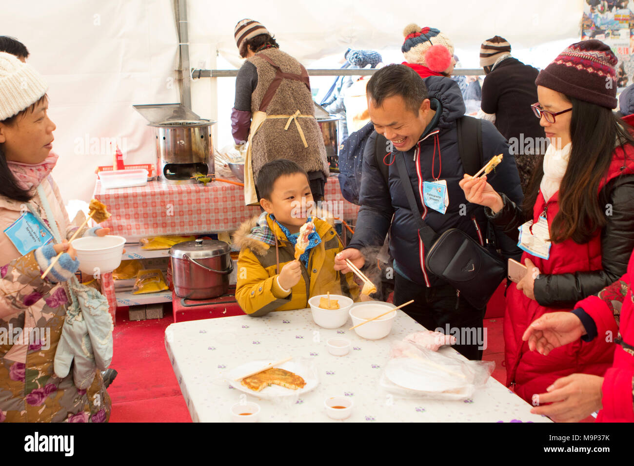 Eine asiatische Familie befindet sich in der Aufwärmphase in einem Zelt, Essen winter Snacks Die Hwacheon Sancheoneo Ice Festival ist eine Tradition für die Menschen in Korea. Jedes Jahr im Januar Menschenmassen versammeln sich auf dem zugefrorenen Fluss der Kälte und dem Schnee des Winters zu feiern. Hauptattraktion ist Eisfischen. Jung und Alt warten geduldig auf ein kleines Loch im Eis für eine Forelle zu beißen. In zelten Sie können den Fisch vom Grill, nach dem sie gegessen werden. Unter anderem sind Rodeln und Eislaufen. Die in der Nähe Pyeongchang Region wird Gastgeber der Olympischen Winterspiele im Februar 2018. Stockfoto