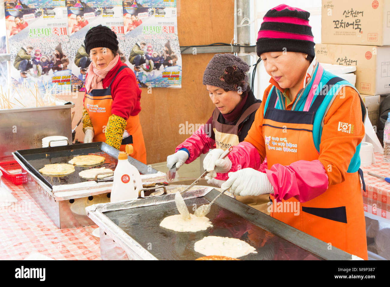 Koreanische Frauen Jeon, koreanisch Pfannkuchen, an der Hwacheon Sancheoneo Ice Festival. Die Hwacheon Sancheoneo Ice Festival ist eine Tradition für die Menschen in Korea. Jedes Jahr im Januar Menschenmassen versammeln sich auf dem zugefrorenen Fluss der Kälte und dem Schnee des Winters zu feiern. Hauptattraktion ist Eisfischen. Jung und Alt warten geduldig auf ein kleines Loch im Eis für eine Forelle zu beißen. In zelten Sie können den Fisch vom Grill, nach dem sie gegessen werden. Unter anderem sind Rodeln und Eislaufen. Die in der Nähe Pyeongchang Region wird Gastgeber der Olympischen Winterspiele im Februar 2018. Stockfoto