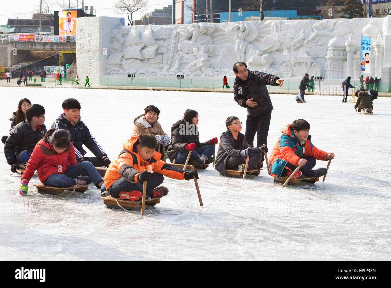 Eine Gruppe der Koreanischen Schule Kinder tun ein Rodeln Wettbewerb. Die Hwacheon Sancheoneo Ice Festival ist eine Tradition für die Menschen in Korea. Jedes Jahr im Januar Menschenmassen versammeln sich auf dem zugefrorenen Fluss der Kälte und dem Schnee des Winters zu feiern. Hauptattraktion ist Eisfischen. Jung und Alt warten geduldig auf ein kleines Loch im Eis für eine Forelle zu beißen. In zelten Sie können den Fisch vom Grill, nach dem sie gegessen werden. Unter anderem sind Rodeln und Eislaufen. Die in der Nähe Pyeongchang Region wird Gastgeber der Olympischen Winterspiele im Februar 2018. Stockfoto