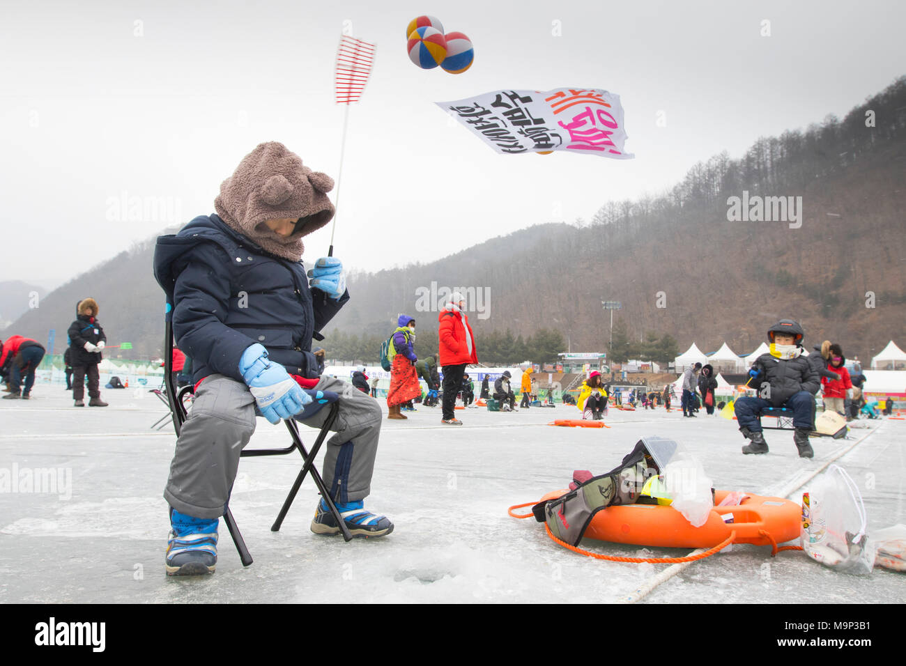 Ein Junge wartet auf ein Loch im Eis im Eis angeln Festival an Hwacheon Sancheoneo in der Region Gangwon-do in Südkorea. Die Hwacheon Sancheoneo Ice Festival ist eine Tradition für die Menschen in Korea. Jedes Jahr im Januar Menschenmassen versammeln sich auf dem zugefrorenen Fluss der Kälte und dem Schnee des Winters zu feiern. Hauptattraktion ist Eisfischen. Jung und Alt warten geduldig auf ein kleines Loch im Eis für eine Forelle zu beißen. In zelten Sie können den Fisch vom Grill, nach dem sie gegessen werden. Unter anderem sind Rodeln und Eislaufen. Die in der Nähe Pyeongchang Region wird Gastgeber der Winter Stockfoto