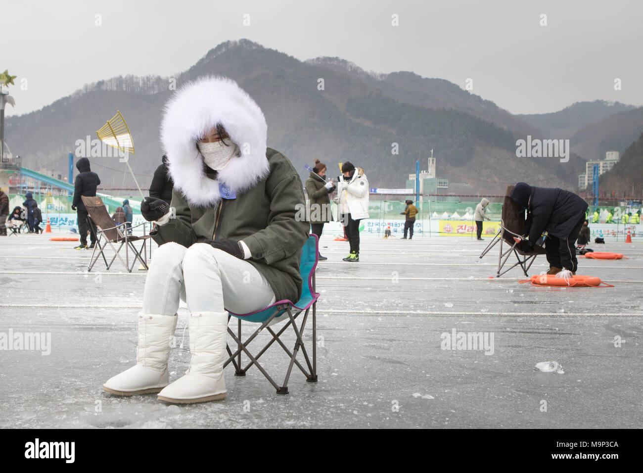 Eine Frau herzlich in einem dicken Fell gekleidet wartet oben ein Loch in das Eis während der Eis angeln Festival an Hwacheon Sancheoneo in der Region Gangwon-do in Südkorea. Die Hwacheon Sancheoneo Ice Festival ist eine Tradition für die Menschen in Korea. Jedes Jahr im Januar Menschenmassen versammeln sich auf dem zugefrorenen Fluss der Kälte und dem Schnee des Winters zu feiern. Hauptattraktion ist Eisfischen. Jung und Alt warten geduldig auf ein kleines Loch im Eis für eine Forelle zu beißen. In zelten Sie können den Fisch vom Grill, nach dem sie gegessen werden. Unter anderem sind Rodeln und Eislaufen. Die in der Nähe Pyeongchang Stockfoto