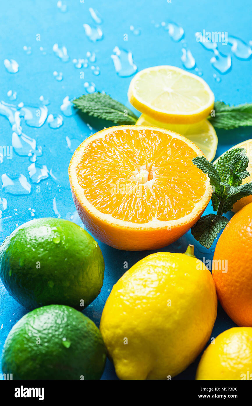 Vielzahl von Zitrusfrüchten Bio-früchten ganz und halbiert Orangen, in Scheiben geschnittene Zitronen Limonen frische Minze auf hellblauem Hintergrund mit Wassertropfen. Morgen Sonnenlicht. Stockfoto