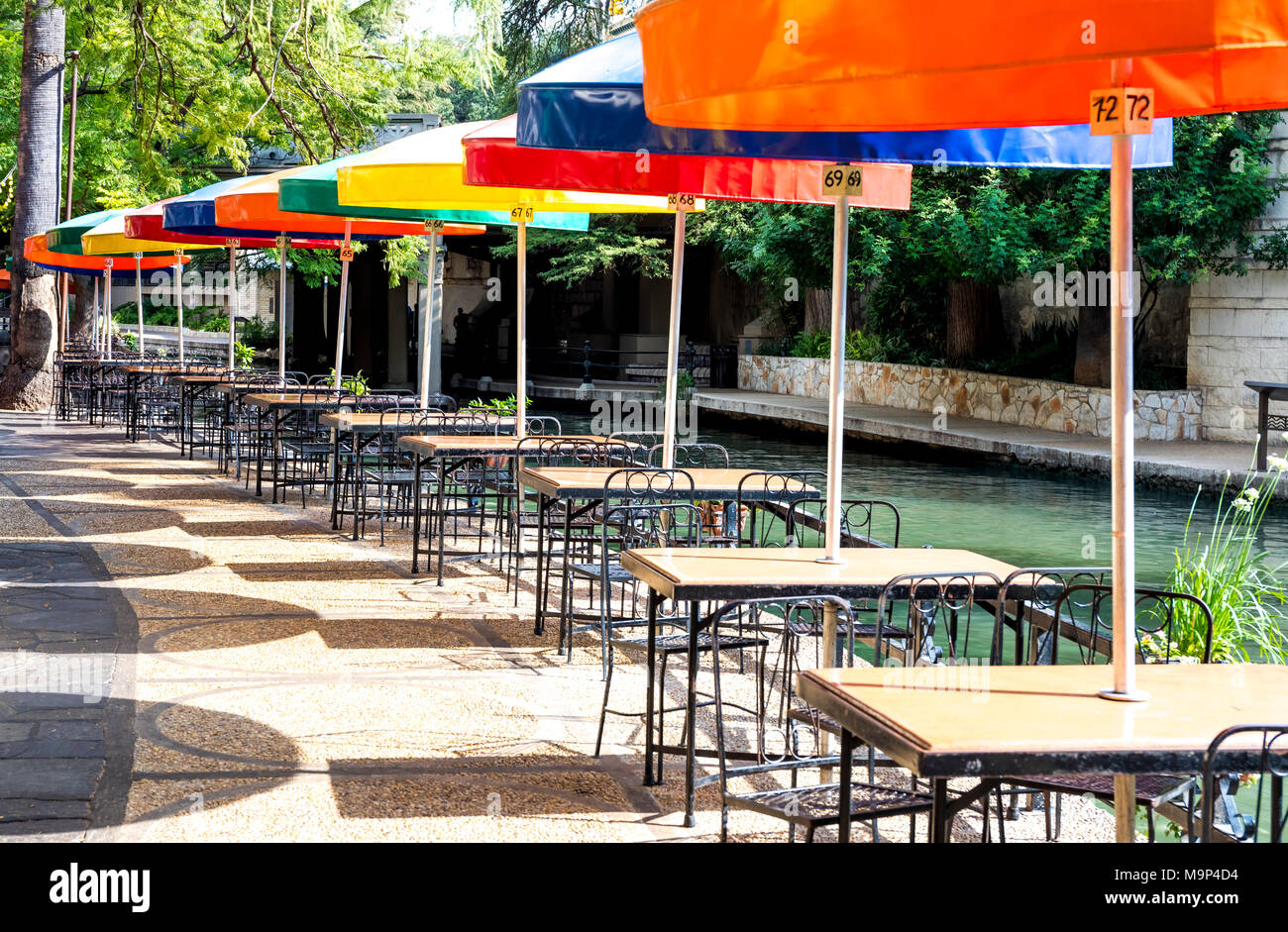 Bunte Sonnenschirme decken Tische in einem Restaurant entlang des San Antonio River Walk auf einer sonnigen Spätsommer Tag. Stockfoto
