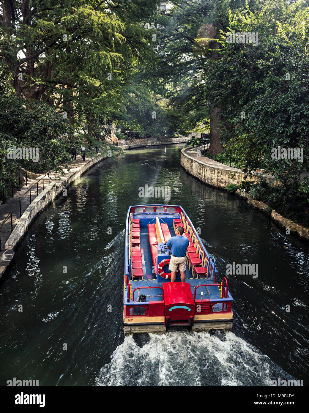 Ein Mann fährt ein Wassertaxi entlang des San Antonio River Walk auf einer sonnigen Spätsommer Tag. Der Riverwalk ist mit Bäumen und sorgt für einen angenehmen ruhigen Ort zu gehen. Stockfoto