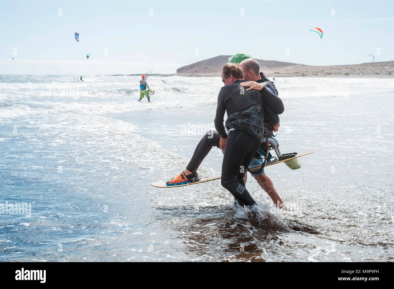 Ein behinderter Kite Surfer wird unterstützt, um das Wasser zu geben Stockfoto