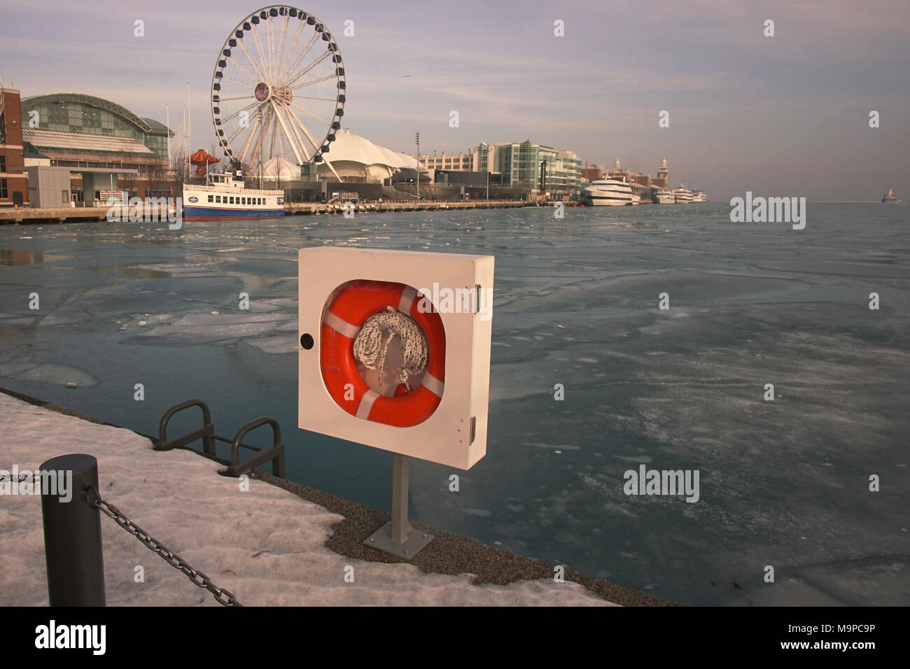 Blick auf das Wasser an einem Wintertag mit Blick auf den Navy Pier und Riesenrad in Distanz, lebensretter Gerät im Vordergrund mit Schnee auf dem Boden Stockfoto