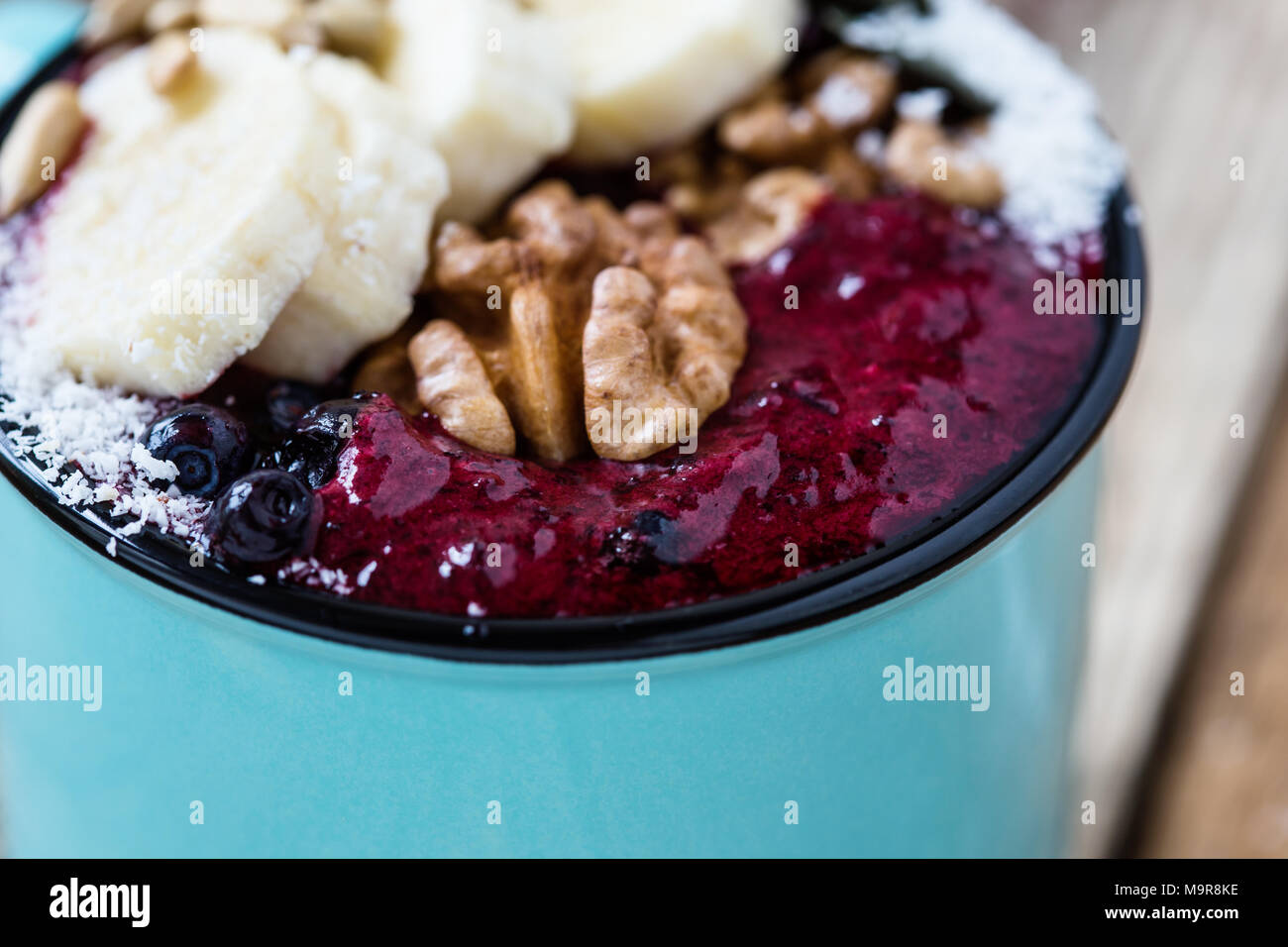 Smoothie Becher mit eingefrorenen Blaubeeren, Bananen, Nüsse, Sonnenblumenkerne und Kokosraspeln auf rustikalen Holztisch Stockfoto