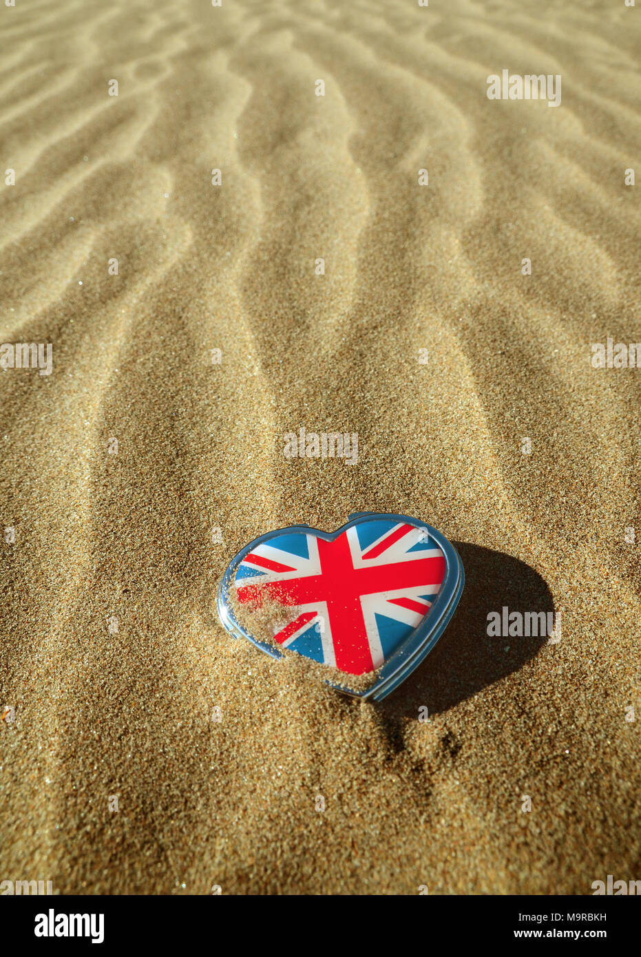 Ein Union Jack mit einem Herzförmigen Dose liegen auf einem sandigen gemusterten Strand. Stockfoto