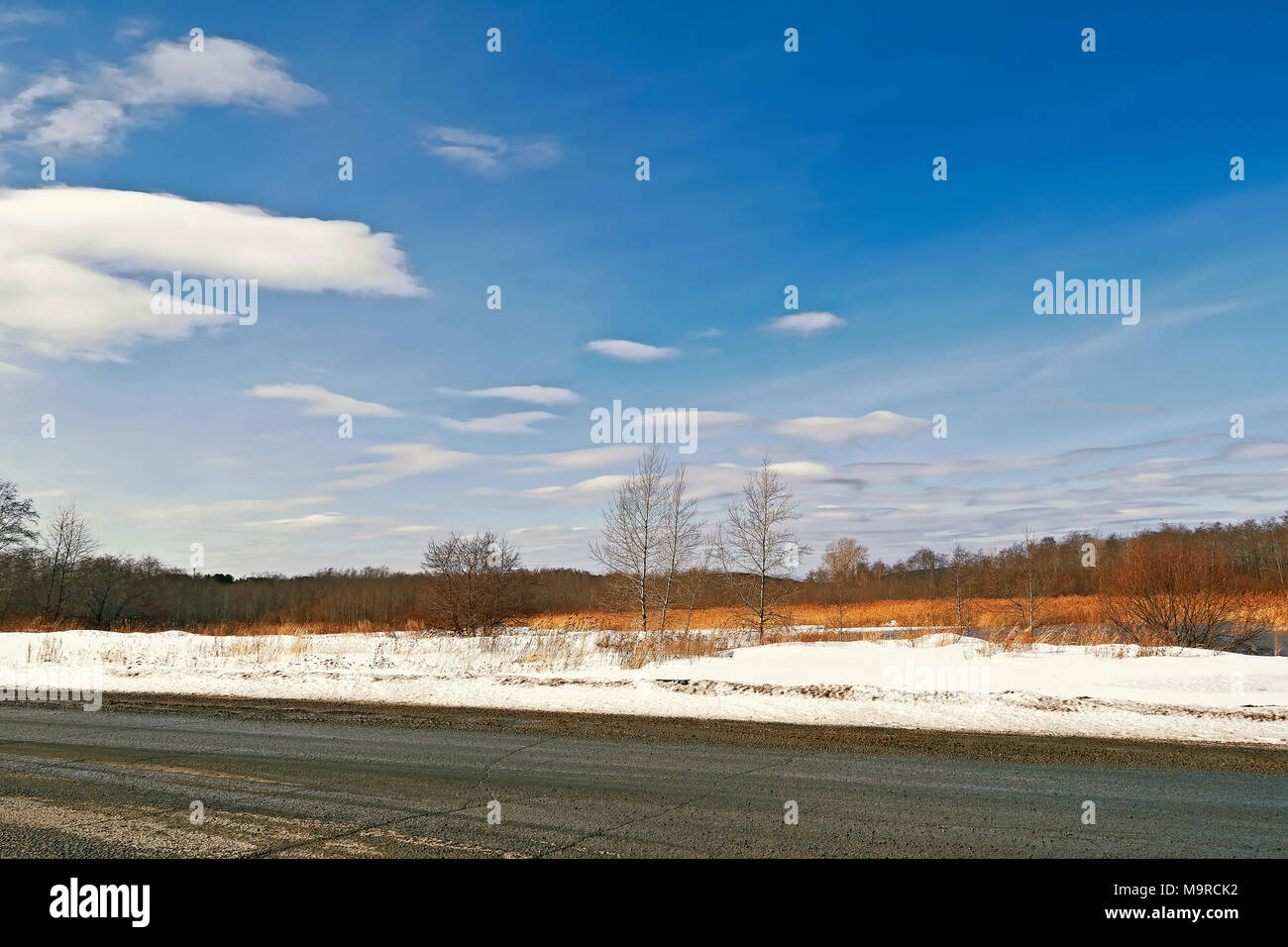 Ländliche Straße durch ein Feld der Schneeschmelze im Frühjahr Stockfoto