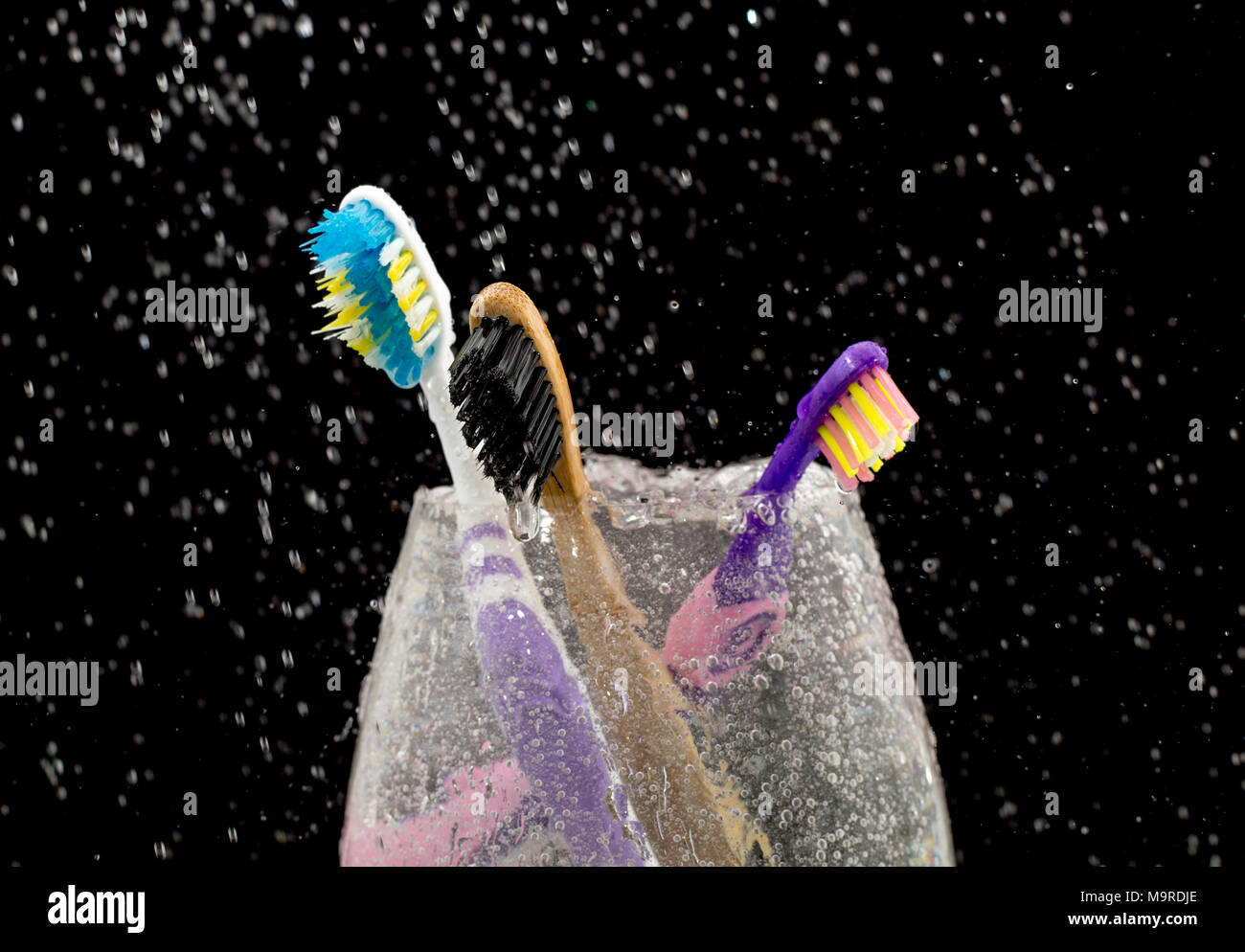 Drei Zahnbürste in ein Glas mit Wasser gefüllt auf einem schwarzen bacground. Stockfoto