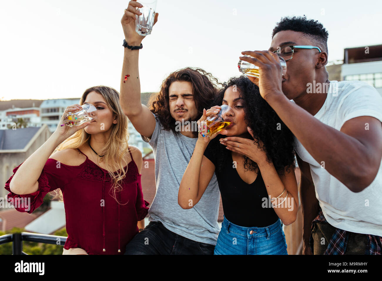 Gruppe von jungen Freunden trinken und genießen einen Abend auf der Dachterrasse. Multirassischen Männer und Frau trinkt auf der Dachterrasse. Stockfoto