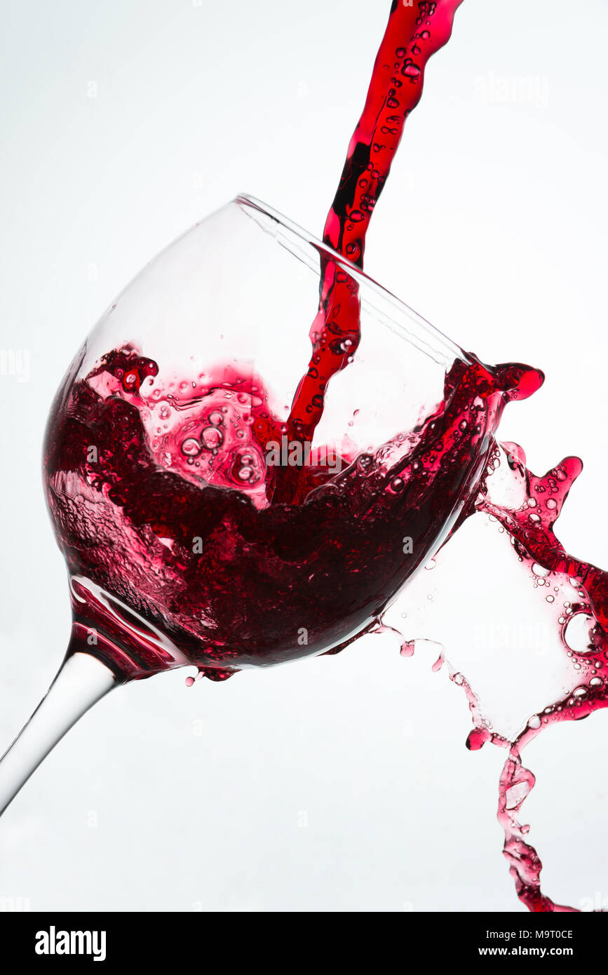 Nahaufnahme von Gießen mit Spill Rotwein auf das Glas vor einen weißen Hintergrund Stockfoto