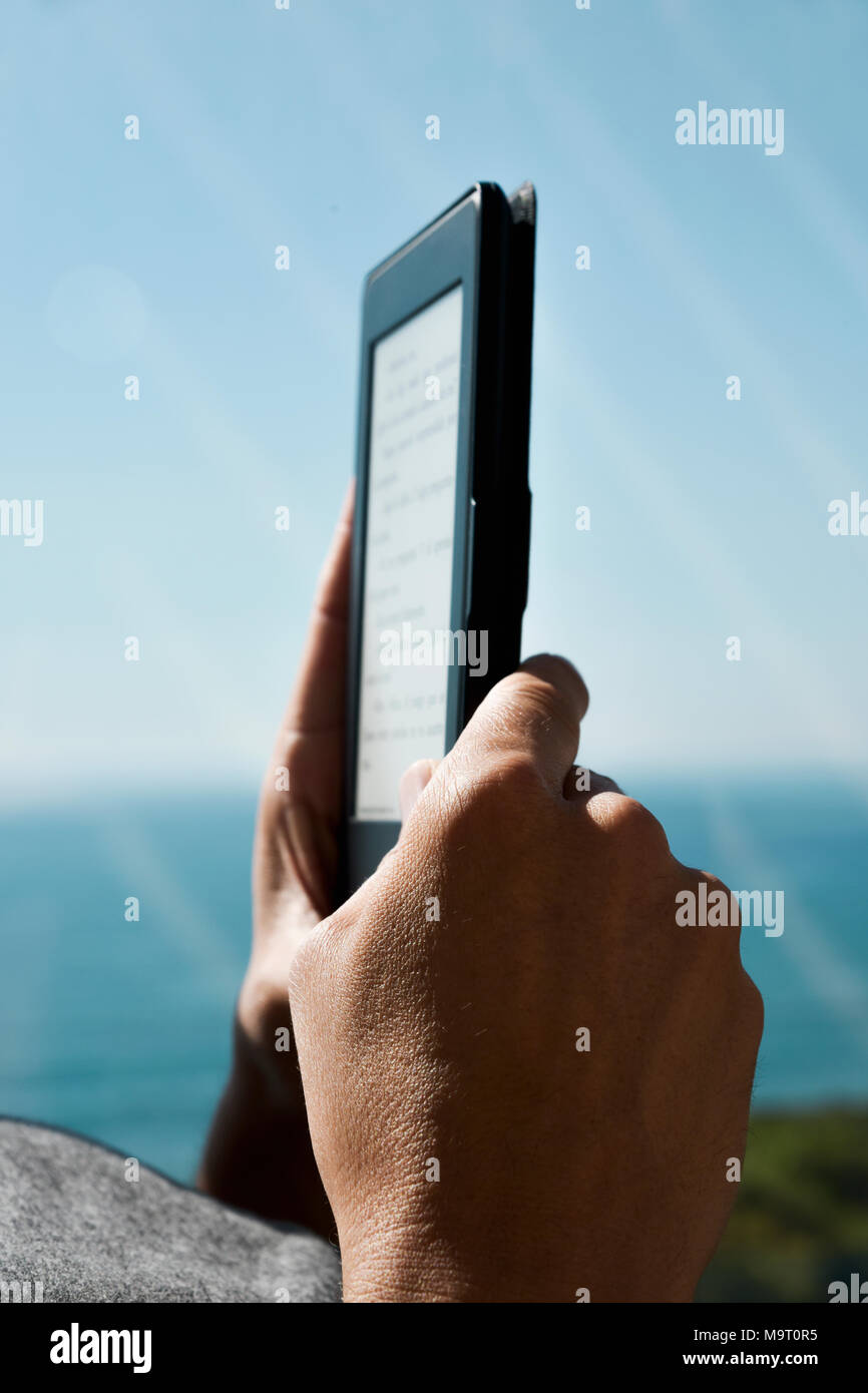 Nahaufnahme eines jungen kaukasischen Mann lesen in einer Tablette oder e-Reader neben einem Balkon Stockfoto