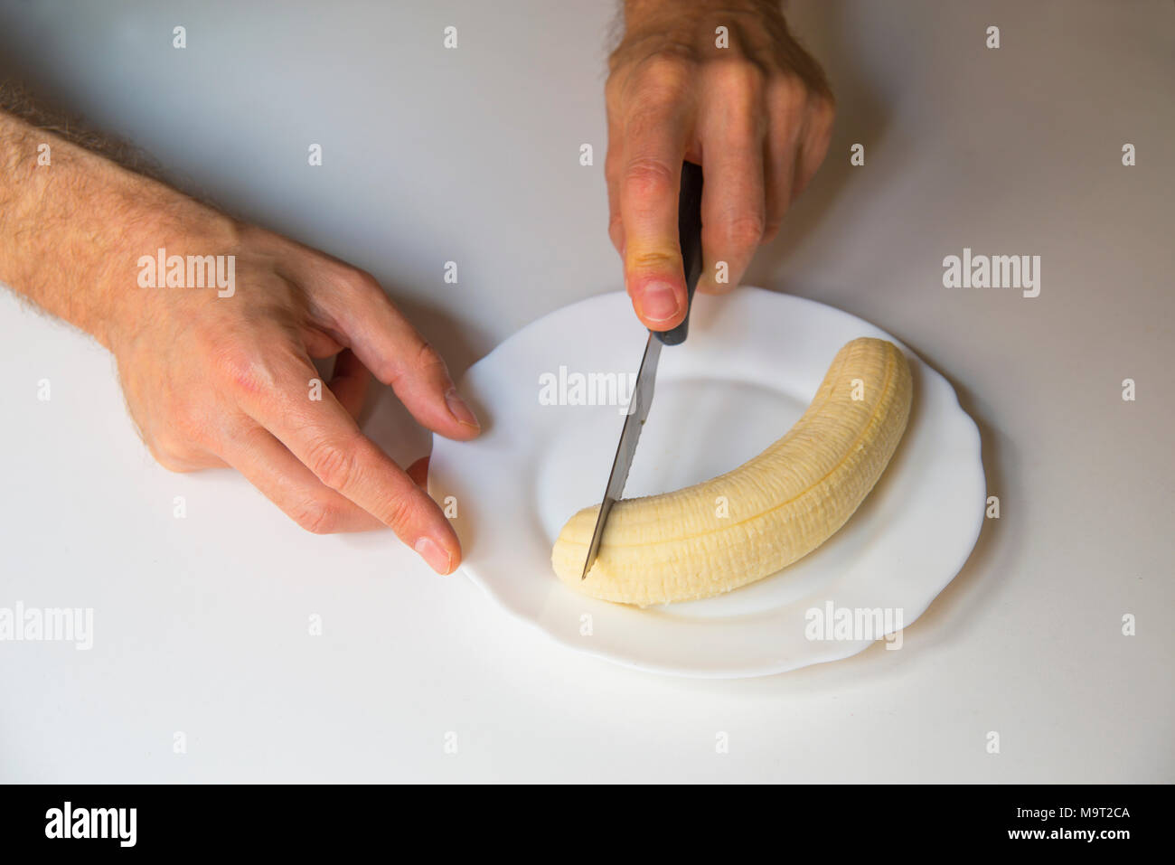 Des Menschen Hand schneiden eine Banane in eine Schüssel. Stockfoto