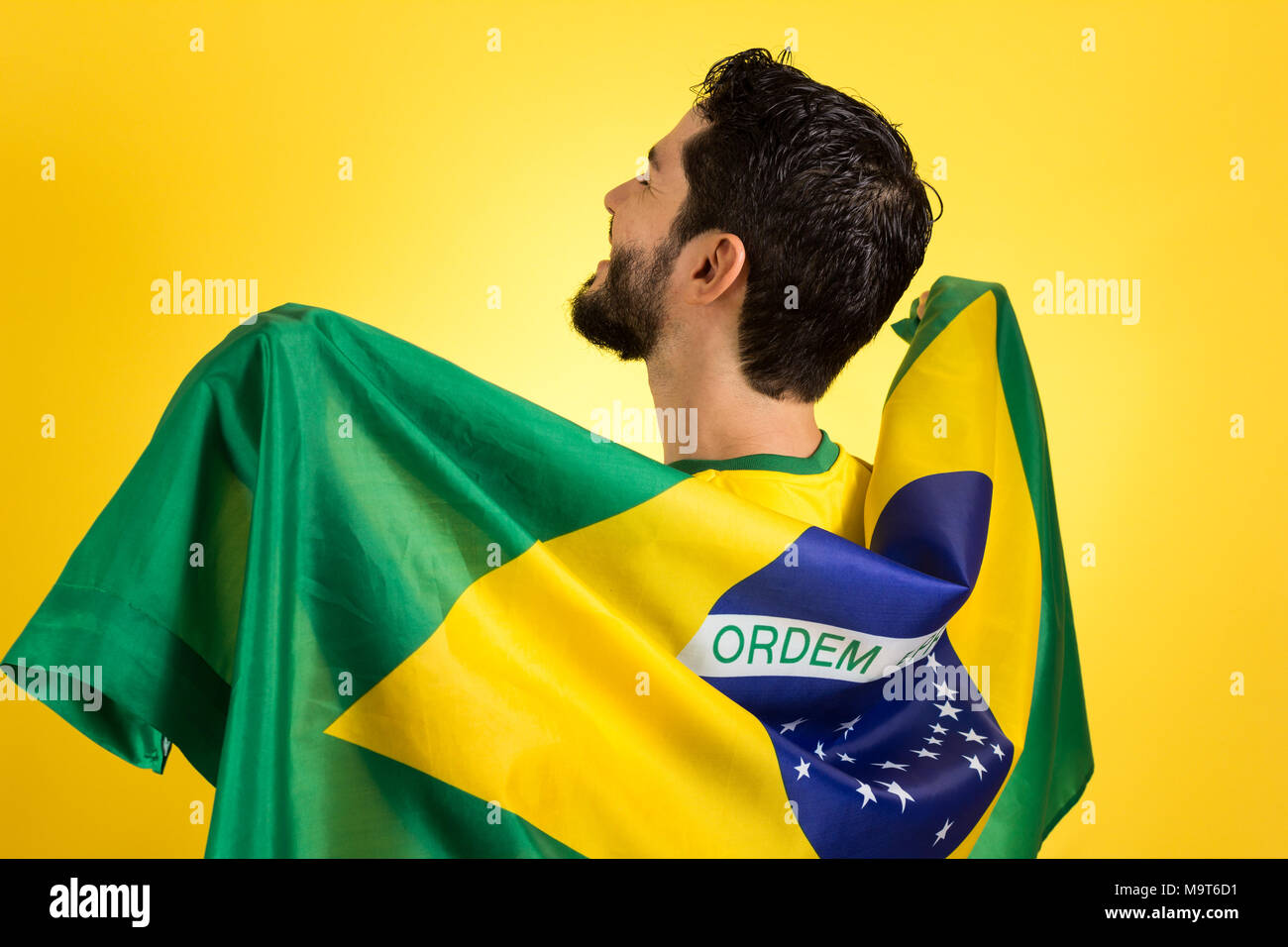 Brasilianischen Fußball-Fußball-Team Player. Ein Unterstützer und Ventilator holding Brasilien Flagge. Tragen gelbe Uniform auf gelben Hintergrund. Stockfoto