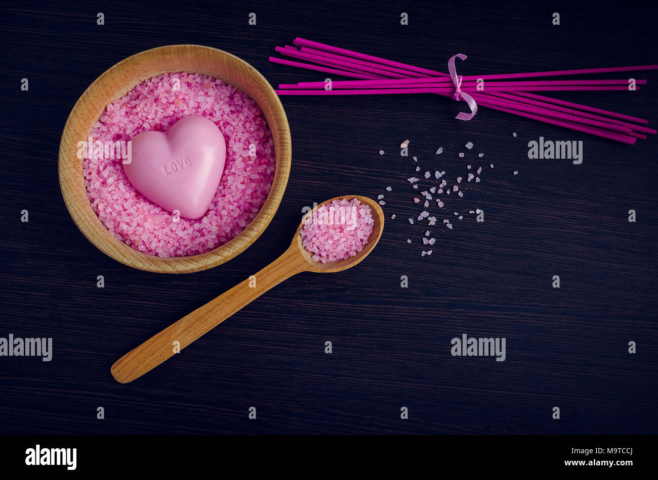 Spa und Wellness Konzept - rosa Meer Salz in die Schüssel mit dem Löffel aus Holz und Seife in Herz Form mit dem Wort Liebe in es auf dunklem Hintergrund. Arom Stockfoto