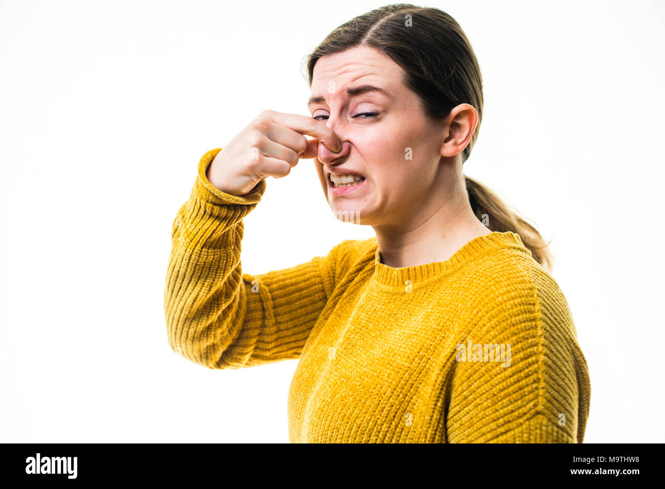 Eine junge Kaukasier Frau Mädchen mit einem gelben Pullover Pullover, Kneifen oder Ihre Nase heraus halten, zu einer schrecklichen übel riechenden Stinkigen schädliche, Umwelt, gegen einen weißen Hintergrund, Großbritannien block Stockfoto