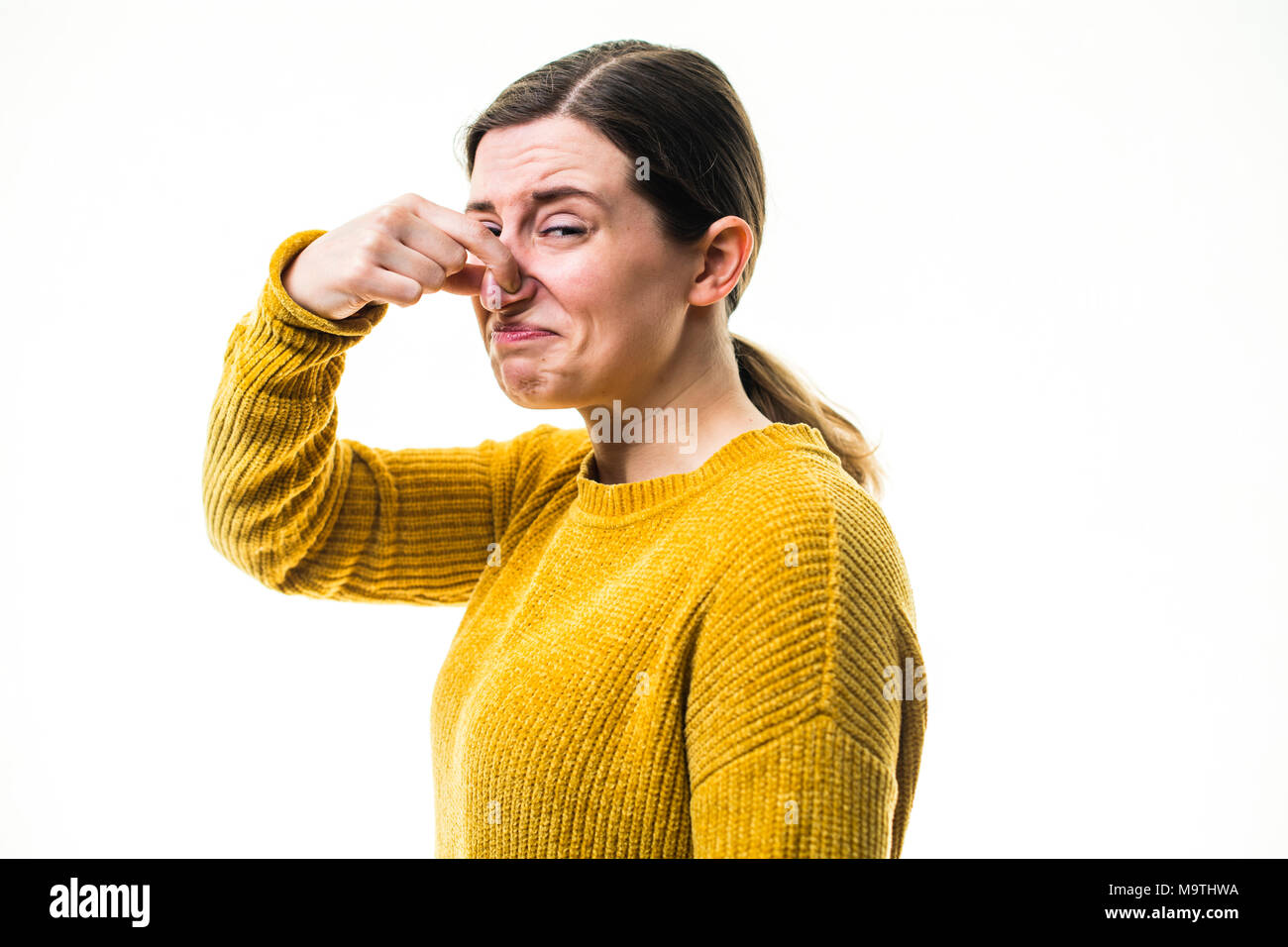 Eine junge Kaukasier Frau Mädchen mit einem gelben Pullover Pullover, Kneifen oder Ihre Nase heraus halten, zu einer schrecklichen übel riechenden Stinkigen schädliche, Umwelt, gegen einen weißen Hintergrund, Großbritannien block Stockfoto