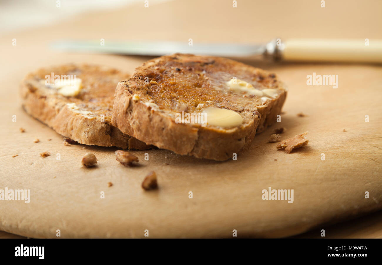 Zwei Scheiben warm nussig Artisan Brot getoastet mit Butter schmelzen auf Holzbrett mit einem Messer aus der Schwerpunkt neben der Schichten. Stockfoto