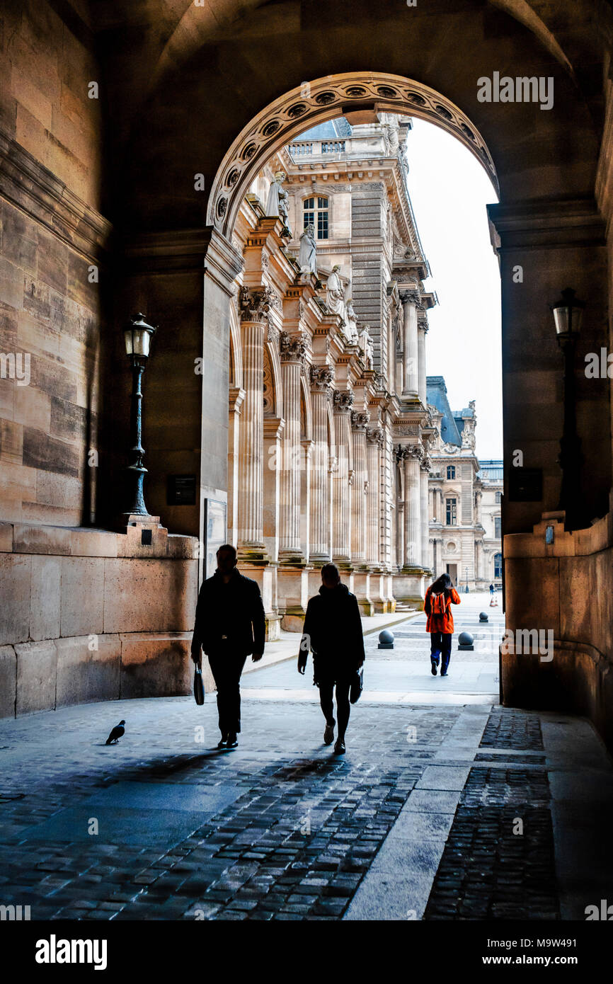 Drei Leute gehen mit Mappen und Taschen zwei voran durch Gang Bogen des Louvre, als Silhouetten Casting Shadows; ein Gefühl der Skala Stockfoto