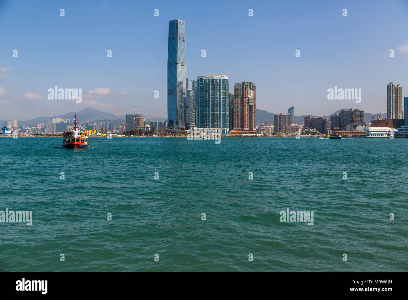 Das International Commerce Center steht stolz in West Kowloon, inmitten der laufenden Bauarbeiten. Eine Fähre überquert den Victoria Harbour zur Hong Kong Insel. Stockfoto