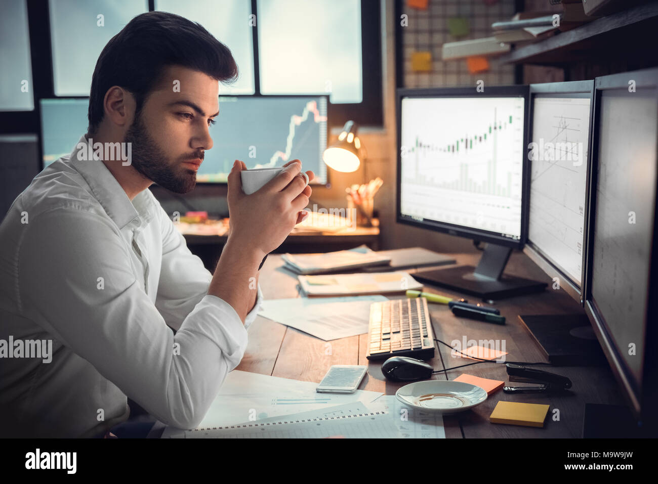 Nachdenklich ernsten Trader broker Kaffee trinken Überstunden am Computer Monitore Analyse stock trading Markt Diagramme, Überlastung, mangelnde o Suchen Stockfoto