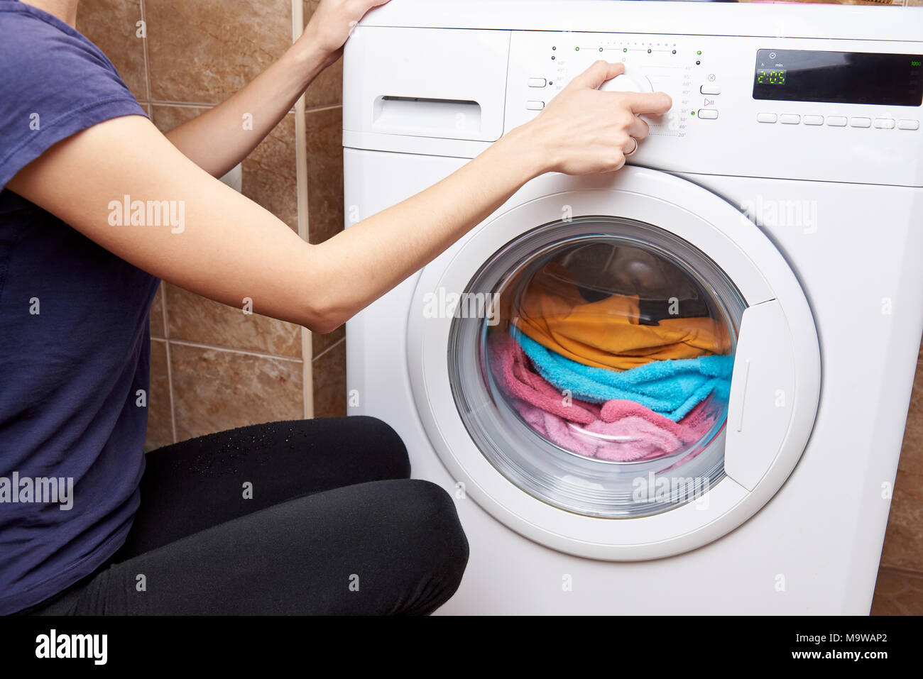 Das Mädchen startet eine Waschmaschine mit farbigen sachen Stockfoto