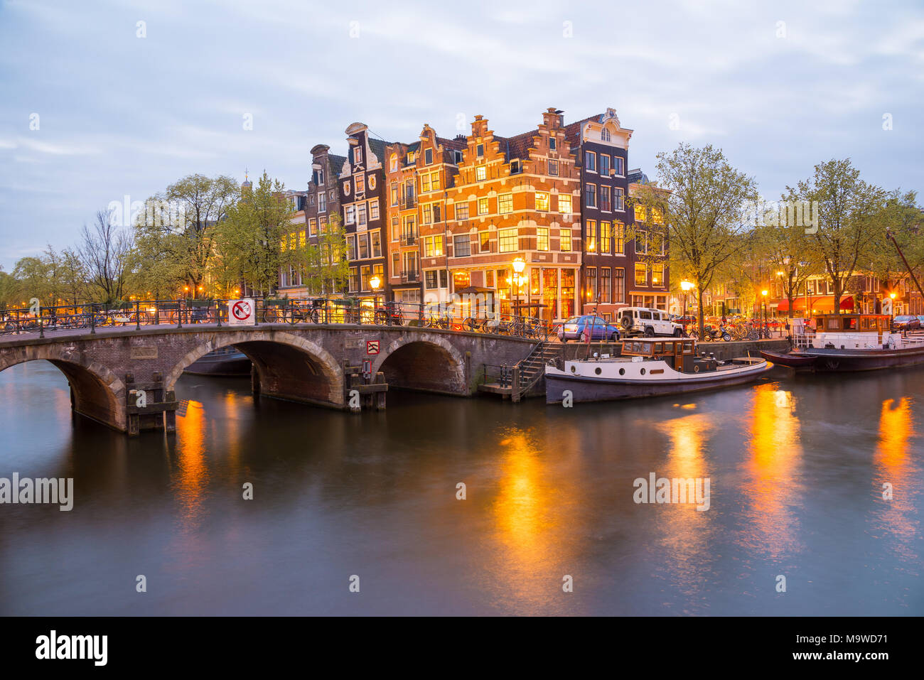 Amsterdam Canal, die Brücke und die typischen Häuser, Boote und Fahrräder in der Abenddämmerung blaue Stunde, Holland, Niederlande. Stockfoto