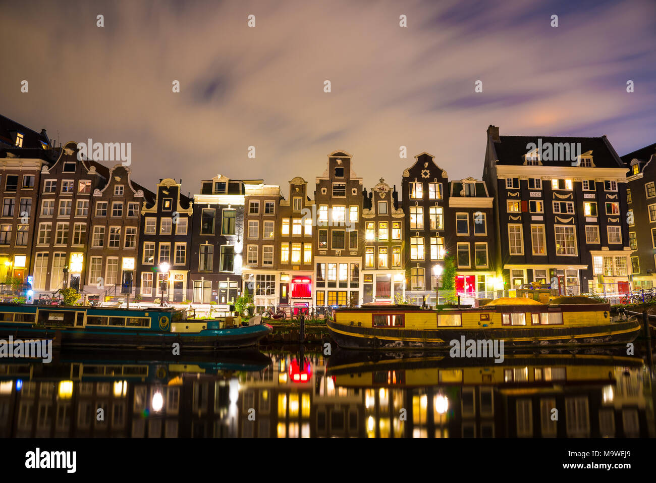 Schöne Nacht in Amsterdam. Nacht Beleuchtung von Gebäuden und Boote in der Nähe der Wasser in den Kanal. Stockfoto