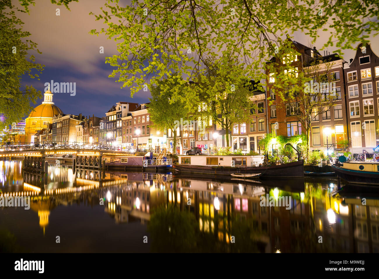 Schöne Nacht in Amsterdam. Nacht Beleuchtung von Gebäuden und Boote in der Nähe der Wasser in den Kanal. Stockfoto