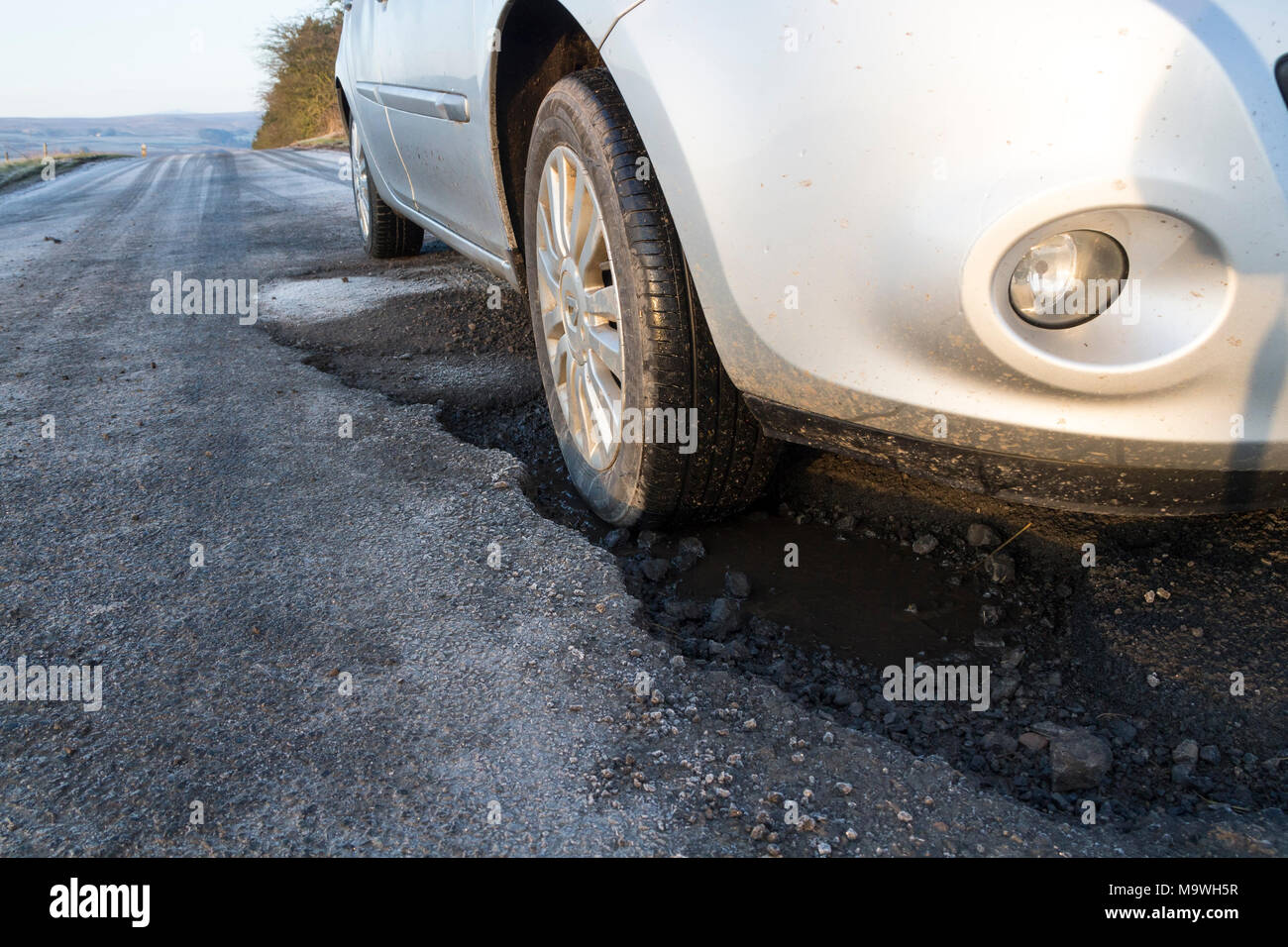 Öffentliche Straße mit einem Fahrzeug in einem tiefen Schlagloch, Teesdale, County Durham, England, UK. Stockfoto