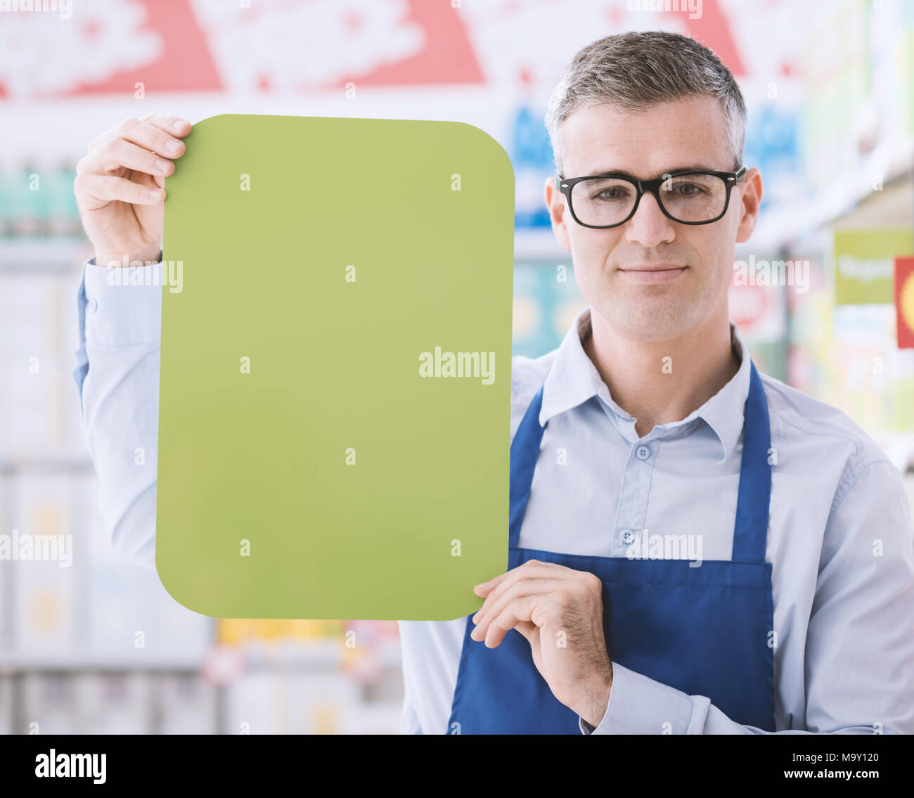 Zuversichtlich Supermarkt Angestellte mit einem grünen leer Zeichen und Kamera, Regale auf dem Hintergrund Stockfoto