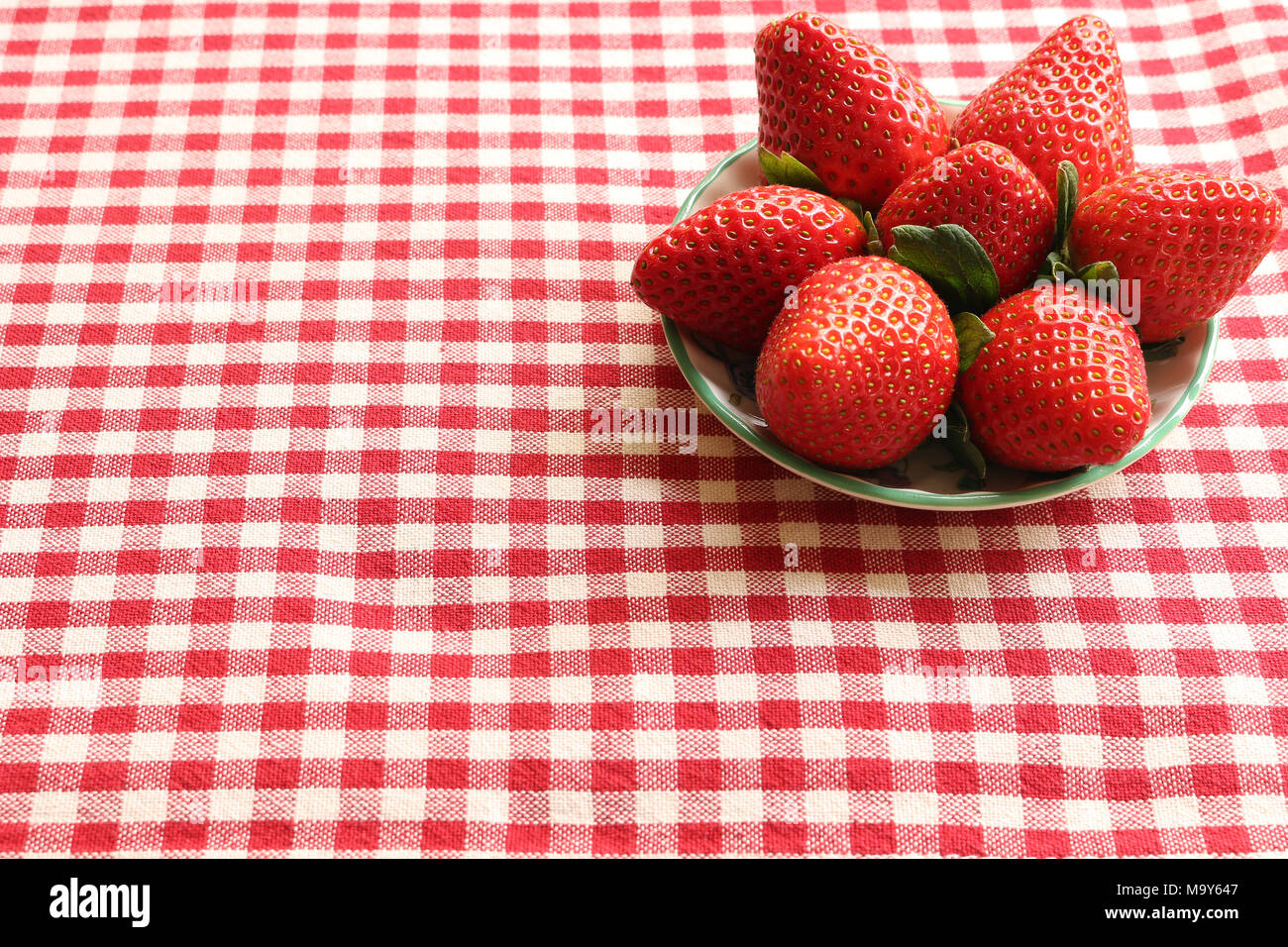 Eine Schüssel Erdbeeren auf rotem gingham Tischdecke Stockfoto