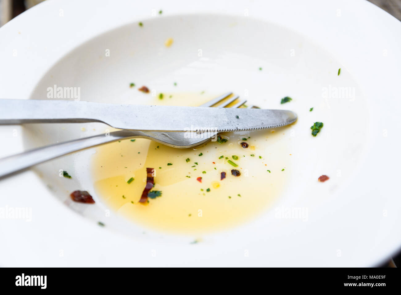 Leere weiße Platte, Messer und Gabel mit Olivenöl, Kräuter und Chiliflocken übrig gebliebene Stockfoto