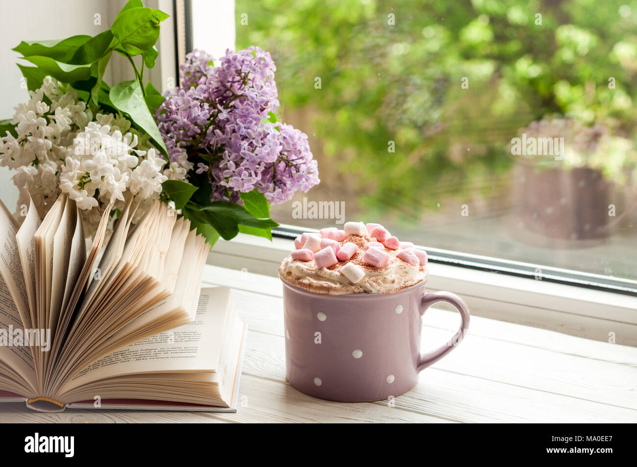 Kaffeetasse mit Eibisch, offenes Buch und Blumen Blumenstrauß auf der Fensterbank. Konzept gemütliches Heim Frühstück und lesen. Sommer oder Frühling Stockfoto