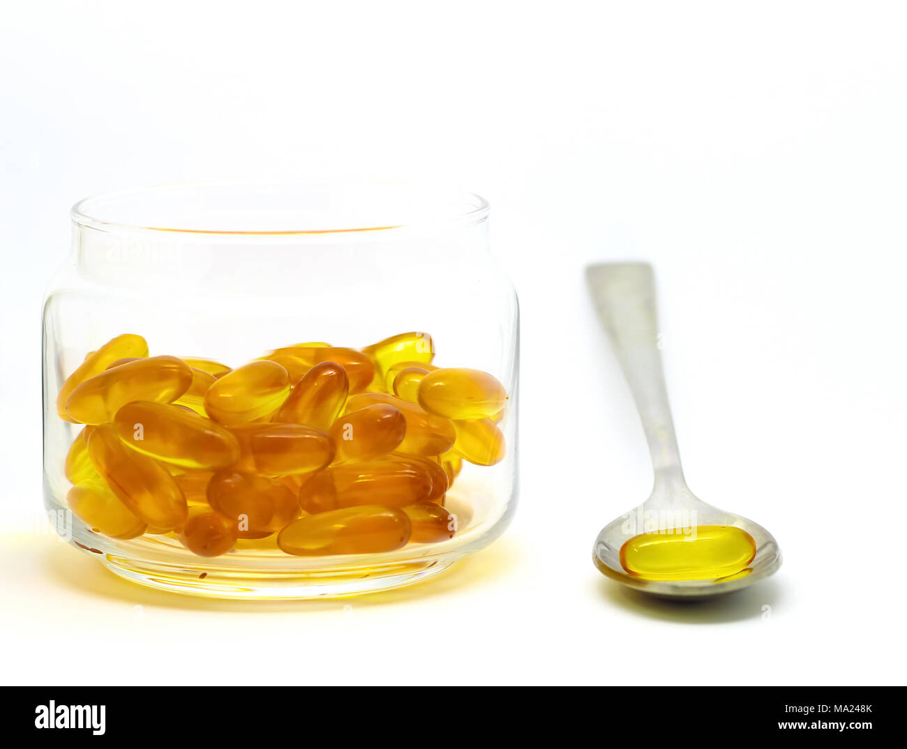 Lebertran Omega 3 Vitamin E Kapseln auf weißem Hintergrund in einem Glasfläschchen isoliert mit Stahl Löffel Stockfoto
