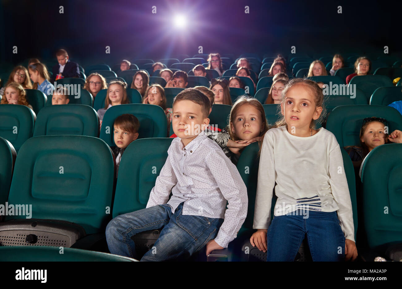 Kleinen Jungen und Mädchen im Kinosaal sitzen, indem Sie neuen Film oder Cartoon. Junge ist auf Kamera, Mädchen schaut Film auf der Kinoleinwand. Andere verlassen, emotionale Kinder für den Hintergrund. Stockfoto