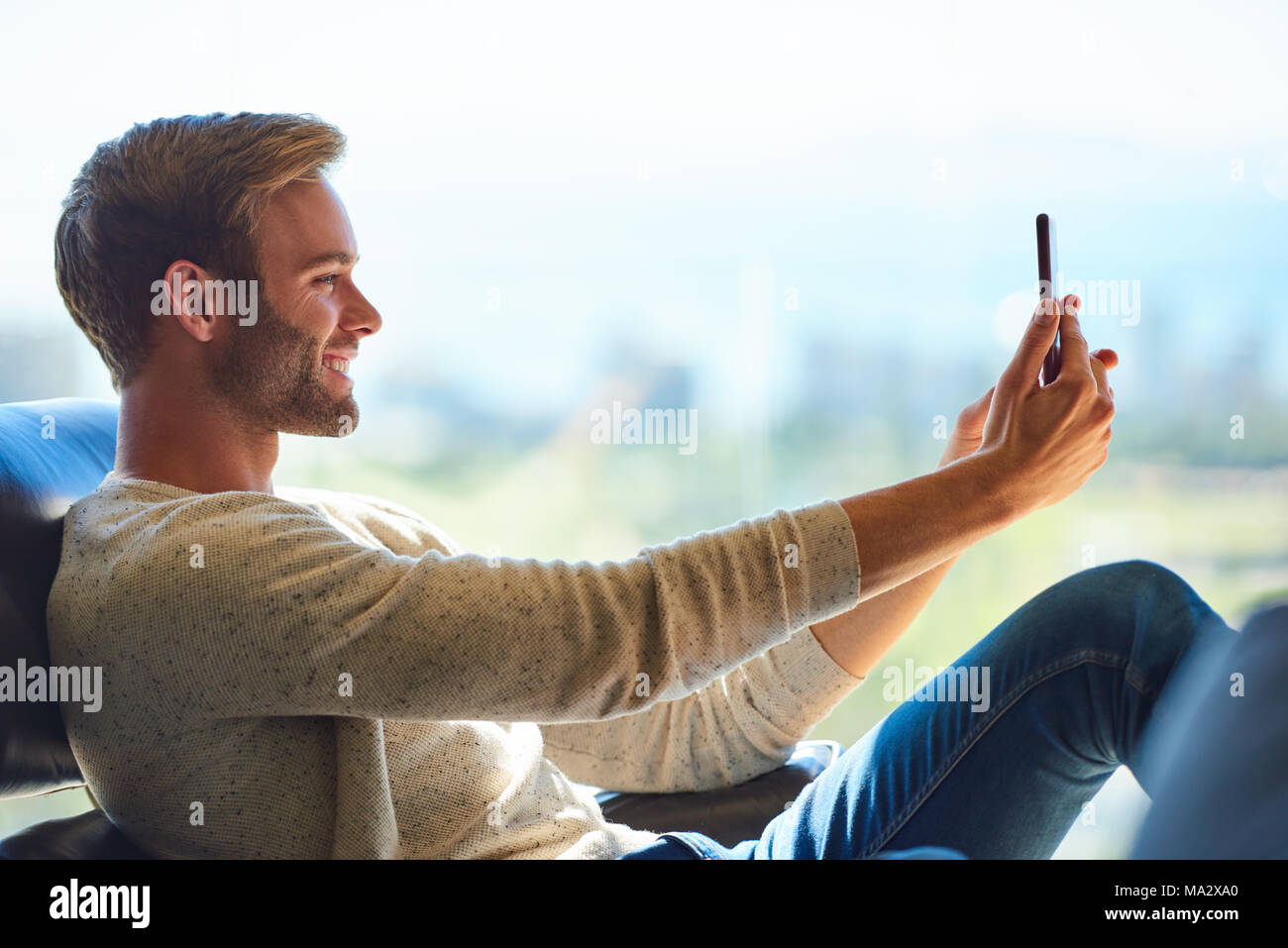 Profil Bild von einem gutaussehenden jungen kaukasischen Mann lächelnd, während Sie einen selfie mit seinem Handy, mit einem wunderschönen Blick auf die Stadt in der Dist Stockfoto