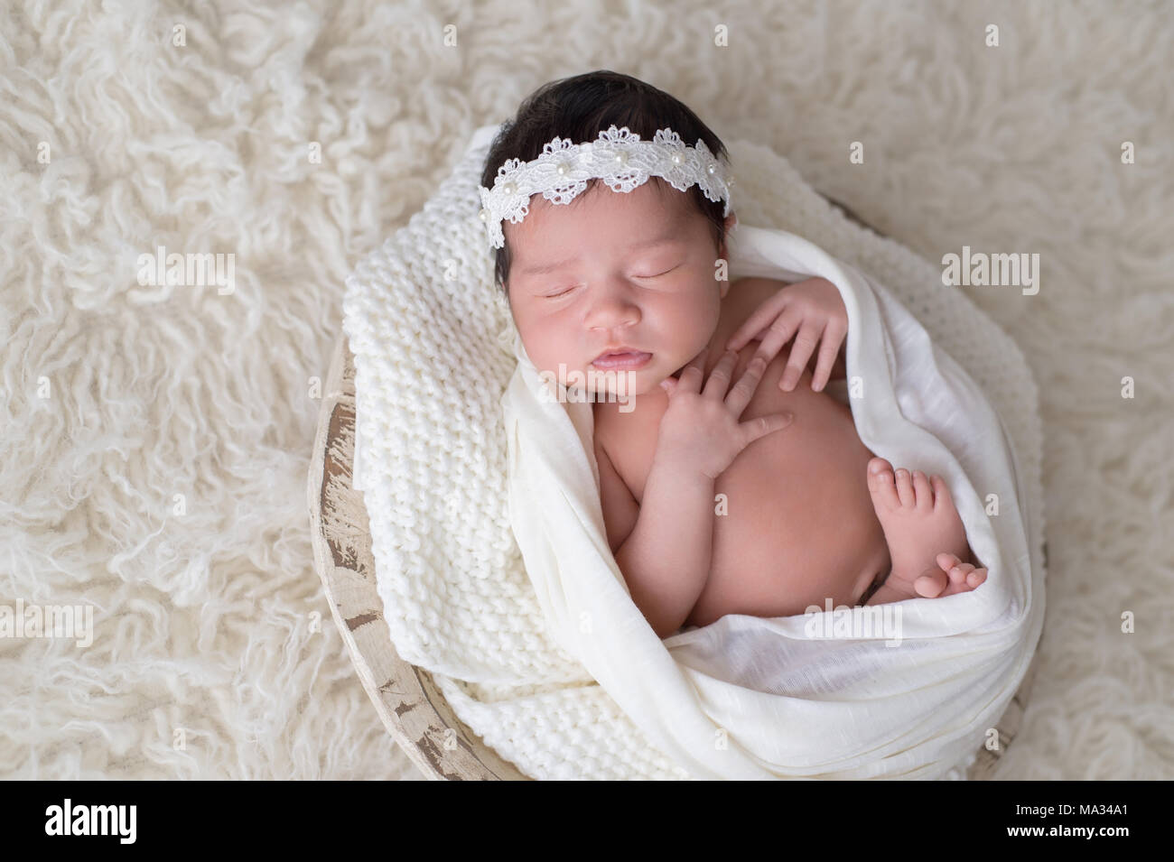 Ein 12 Tage altes Baby Mädchen in eine kleine, hölzerne Schüssel schlafen. Sie trägt ein weißes, Spitze und Pearl Stirnband. Im Studio gedreht auf einem weißen floak Stockfoto