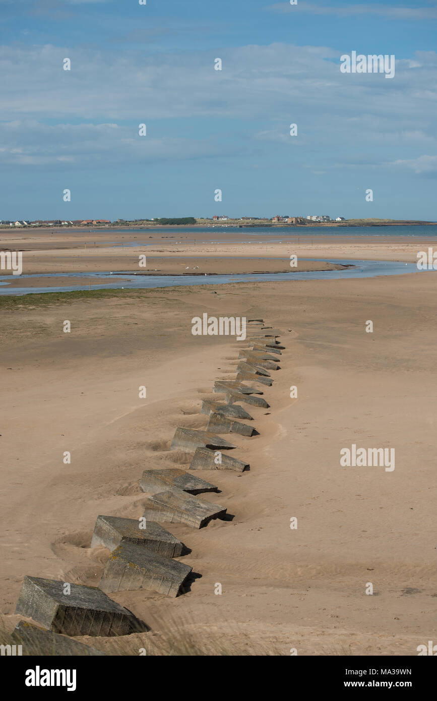Eine Strandszene mit Beadnel, Northumberland im Hintergrund und eine Schnur aus dem zweiten Weltkrieg zwei Betontankfallen, die in den Sand eingebettet sind Stockfoto