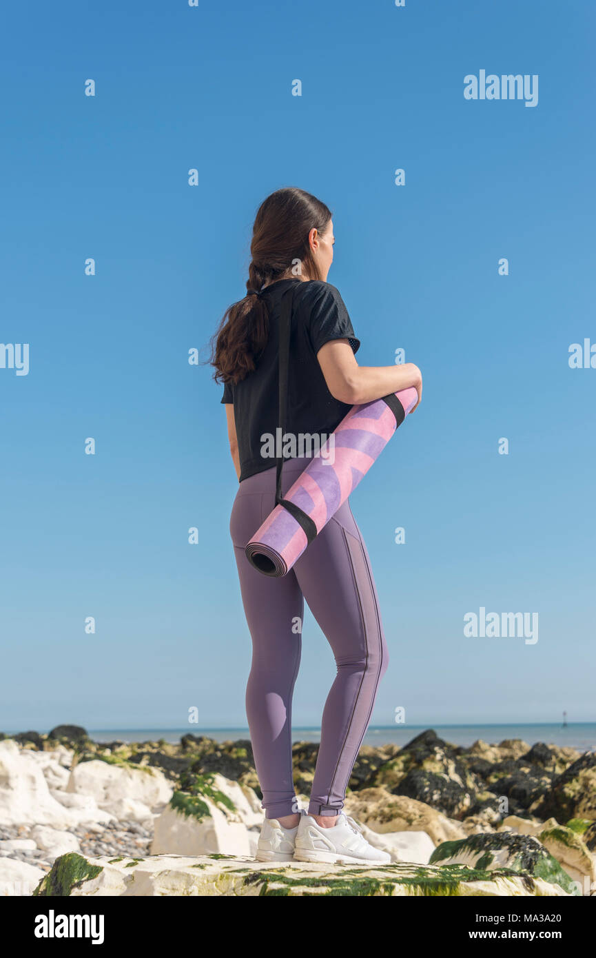 Rückansicht einer Frau mit einem Zusammengerollten Yogamatte mit blauer Himmel Stockfoto