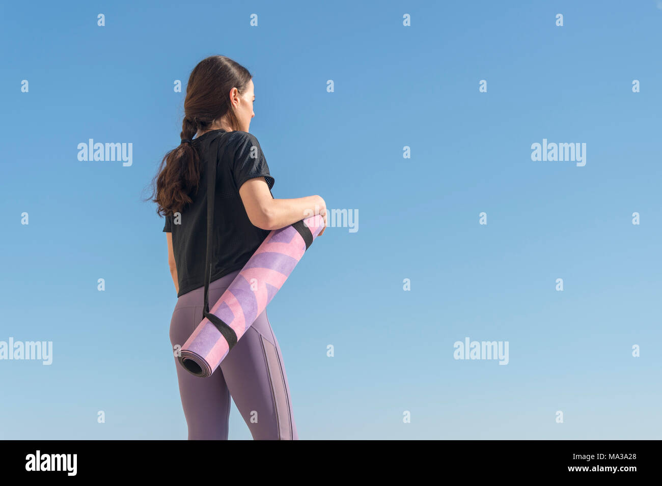 Rückansicht einer Frau mit einem Zusammengerollten Yogamatte mit blauer Himmel Stockfoto