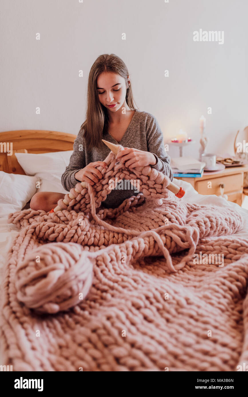 Junge Frau im Bett sitzen und stricken mit XXL Wolle Stockfoto