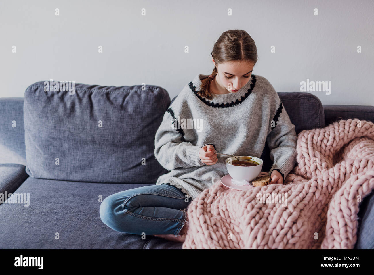 Junge Frau sitzt auf einem Sofa und Essen eine Suppe Stockfoto