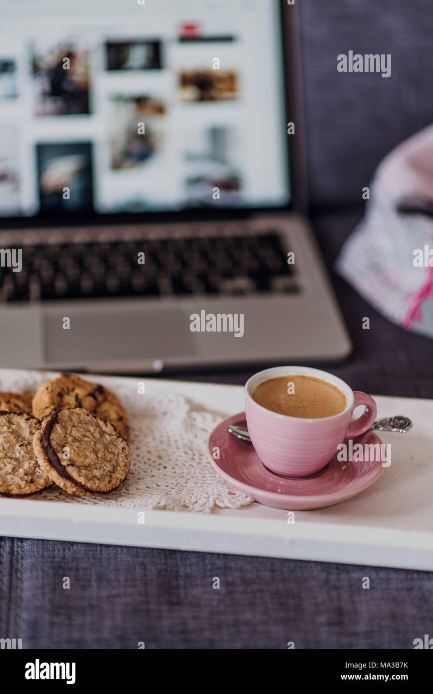 Tablett mit Kaffee und Plätzchen vor dem Laptop auf der Couch Stockfoto