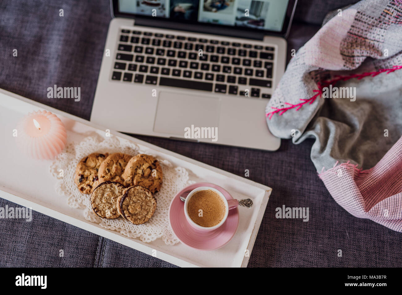 Tablett mit Kaffee, Kekse und Kerzen vor dem Laptop auf der Couch Stockfoto