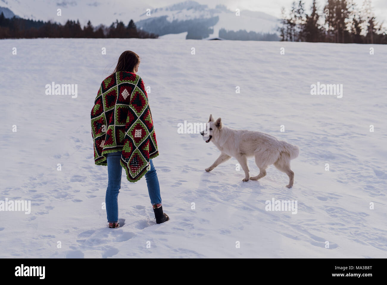 Junge Frau in eine Decke gewickelt ist, stehen im Schnee, Schäferhund spielt mit einem Ball, Stockfoto