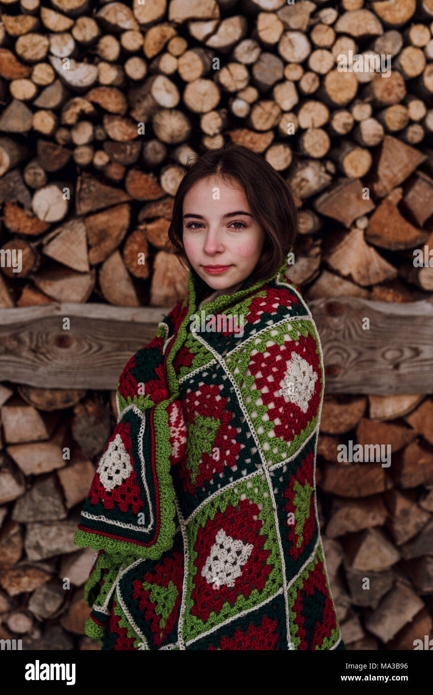 Junge Frau in eine Decke vor einem Woodpile gewickelt, Porträt Stockfoto